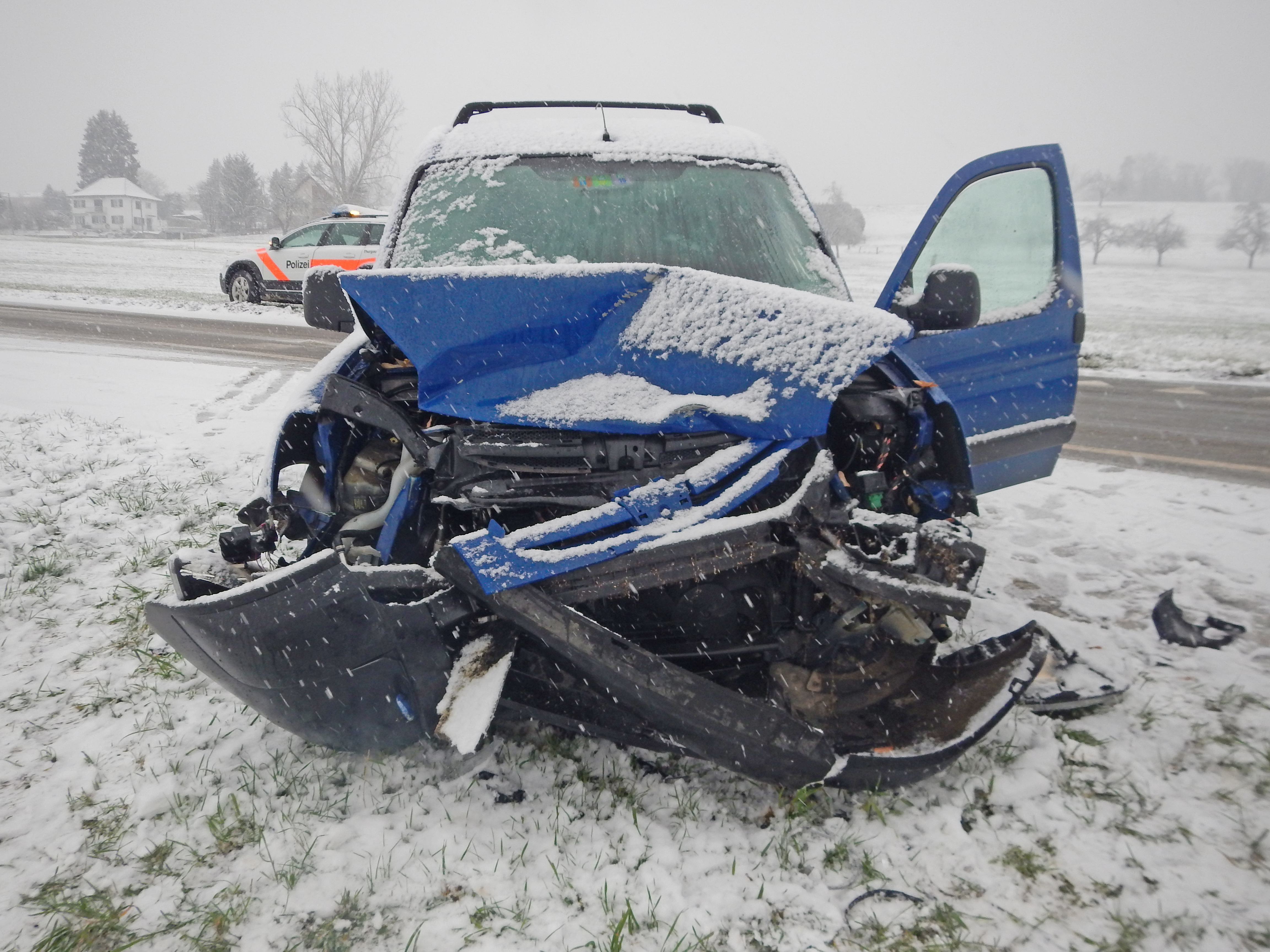 Fahrzeug mit Totalschaden, schneebedeckte Strasse, im Hintergrund ein Polizeifahrzeug.