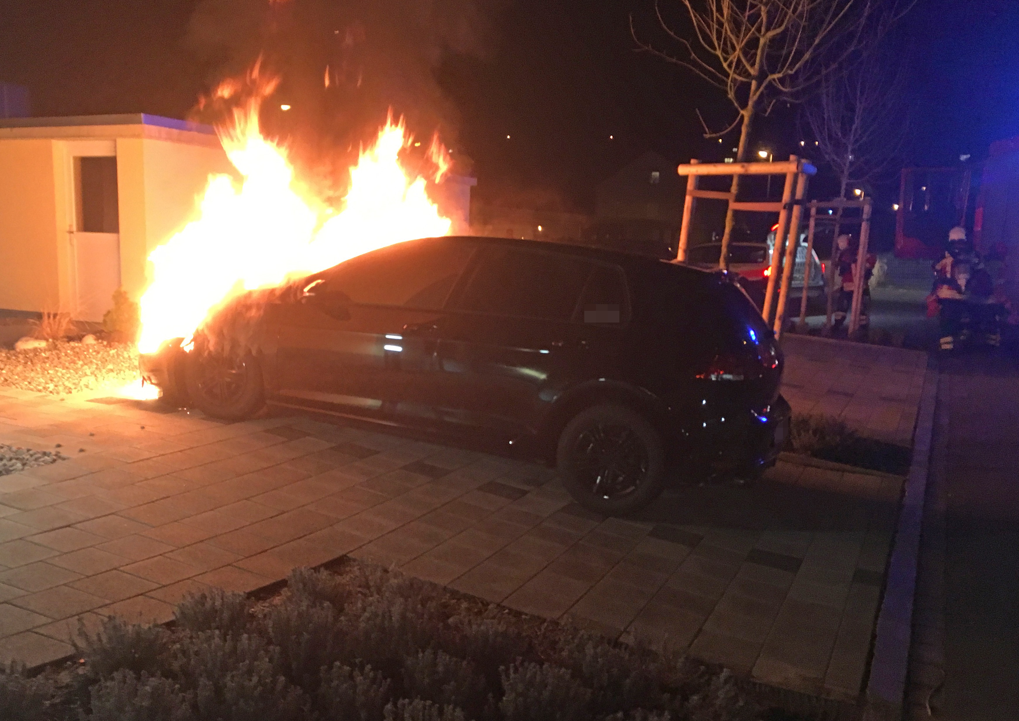 Brennendes Auto, im Hintergrund Polizei und Feuerwehr.