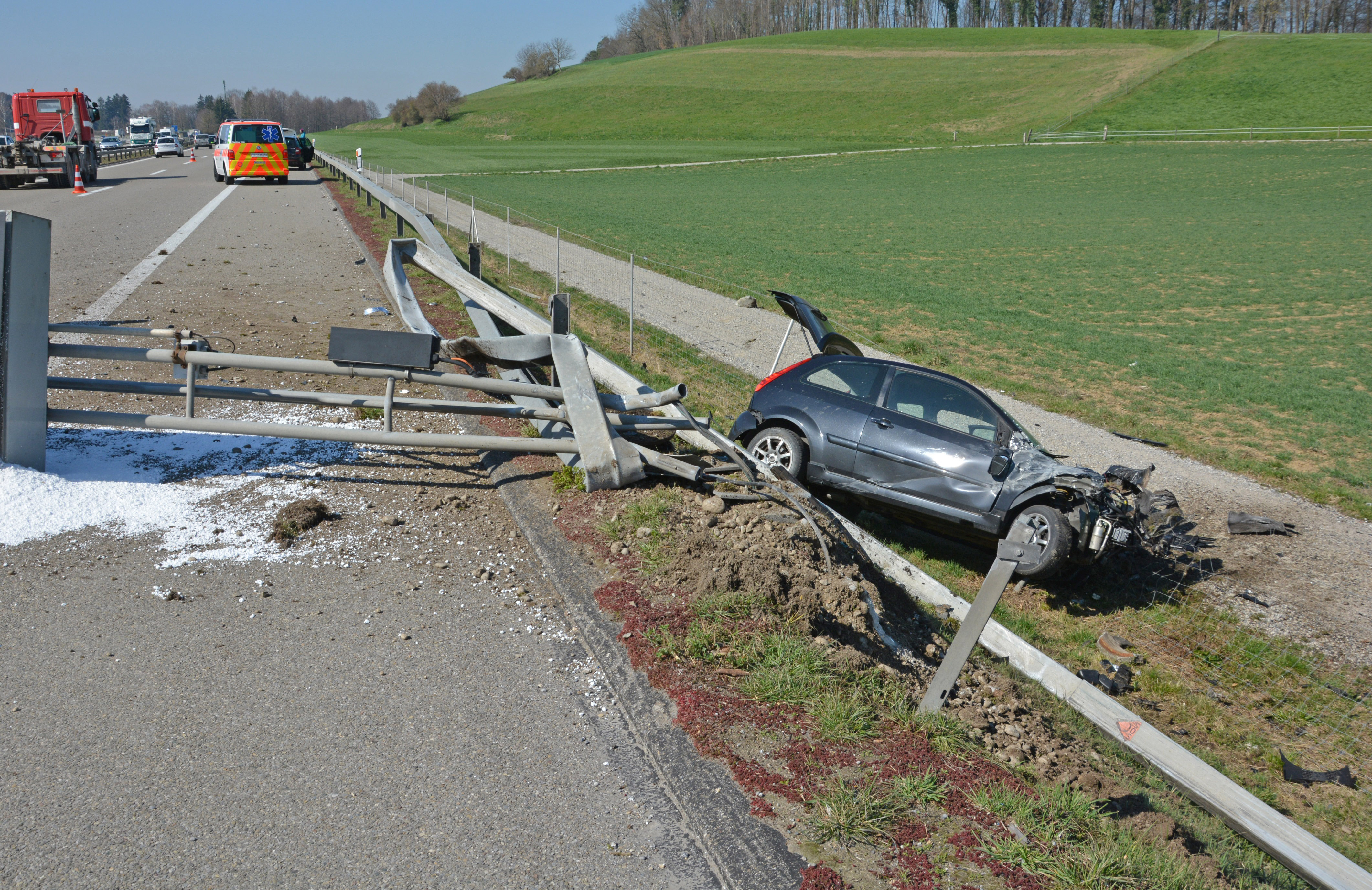 Stark beschädigte Autobahneinrichtung und Fahrzeug auf der Seite liegend im Wildzaun.