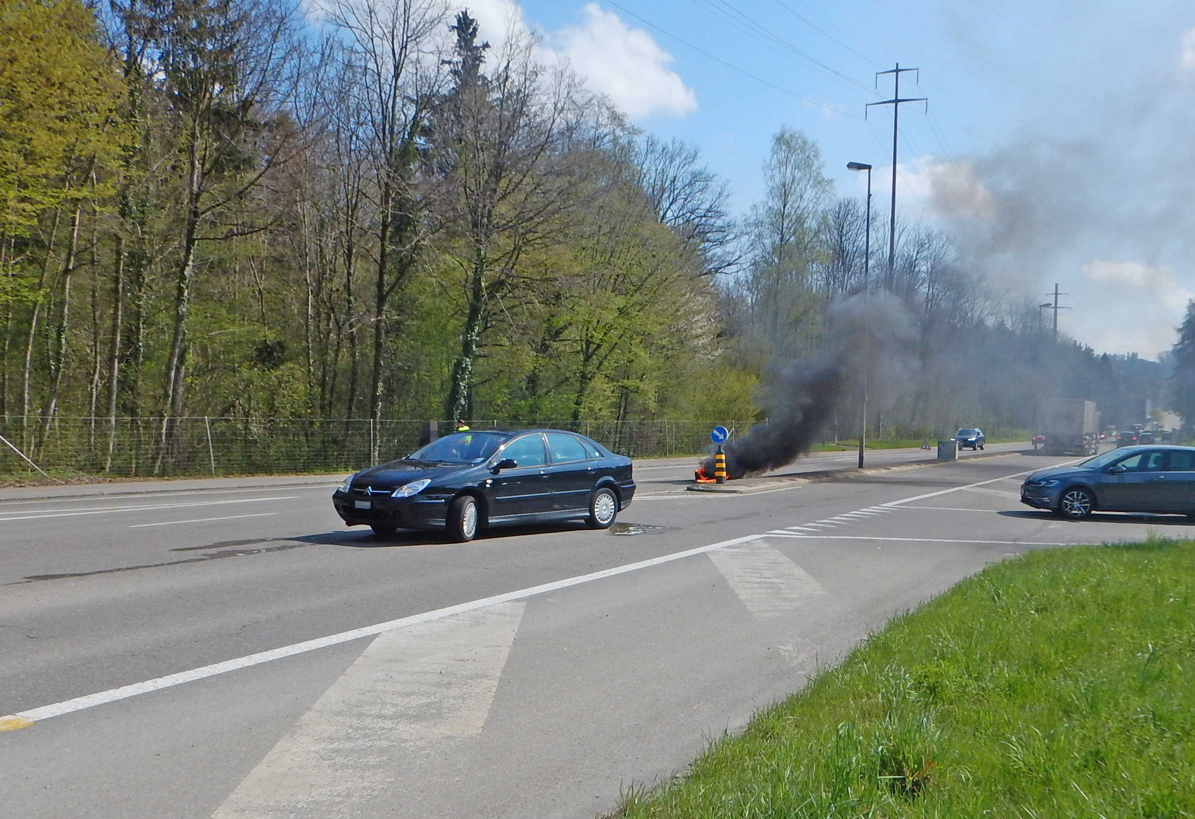 Motorrad im Verzweigungsbereich das brennt, im Hintergrund das Fahrzeug des Unfallverursachers.